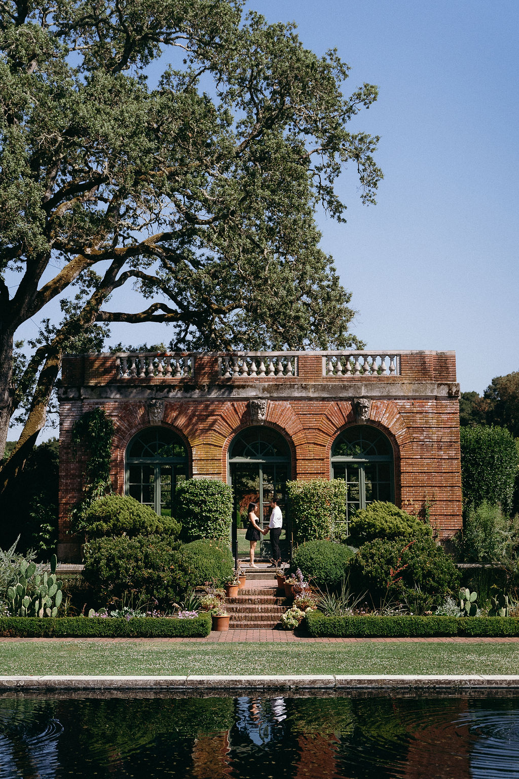 Wide view of the couple standing outside the garden house at Fioli Gardens