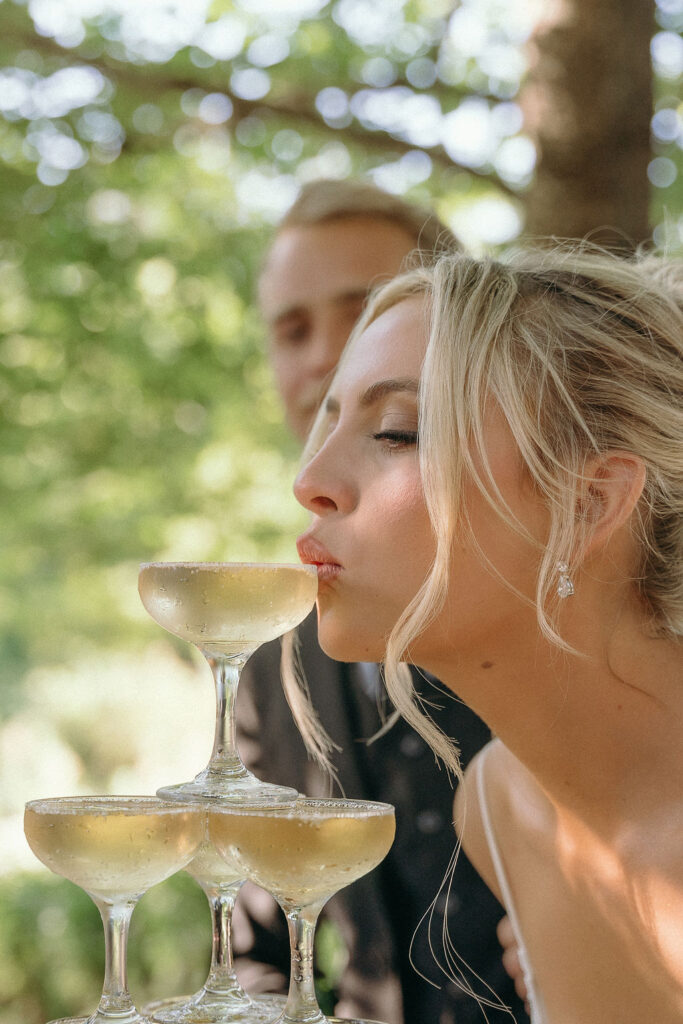 Bride playfully kisses the top glass of a champagne tower at a Mendocino wedding.