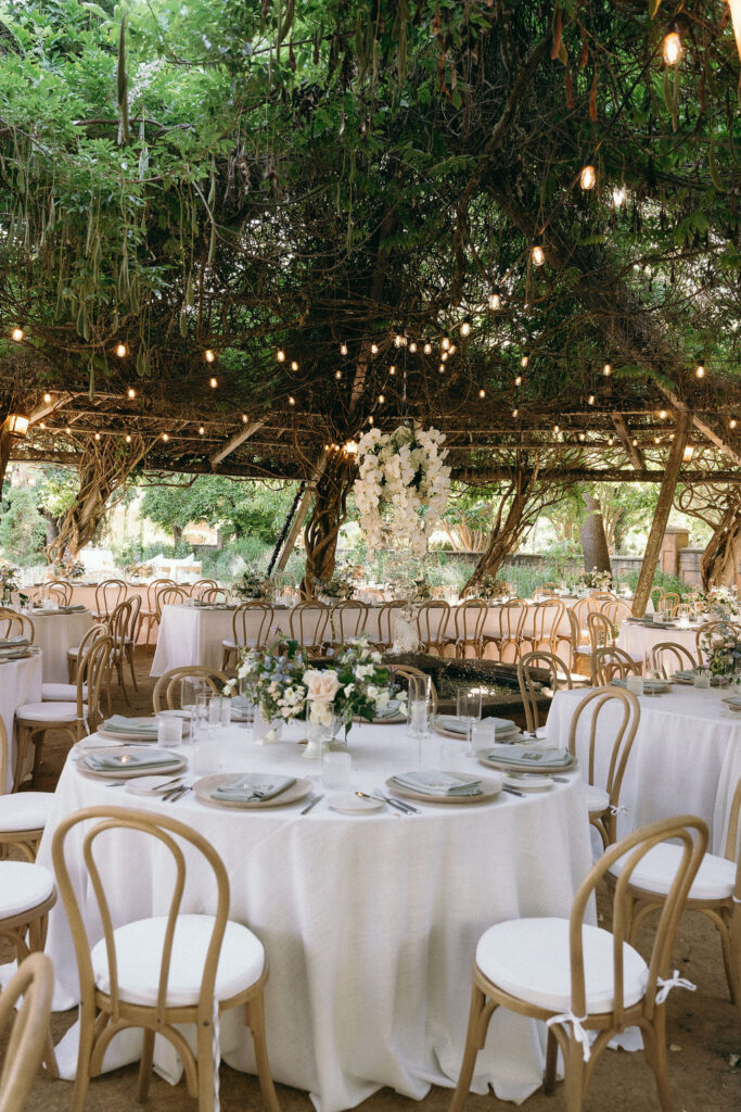 Elegant outdoor wedding reception setup with round tables under a vine-covered pergola in Mendocino.