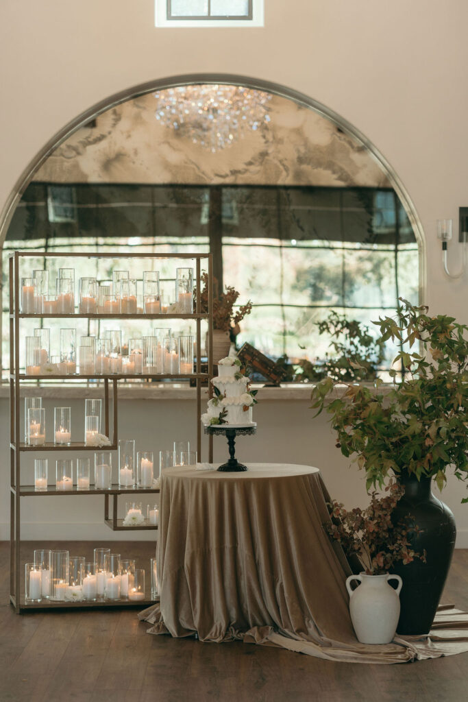 Wide shot of a three-tier wedding cake with floral accents and candles at Monserate Winery wedding reception