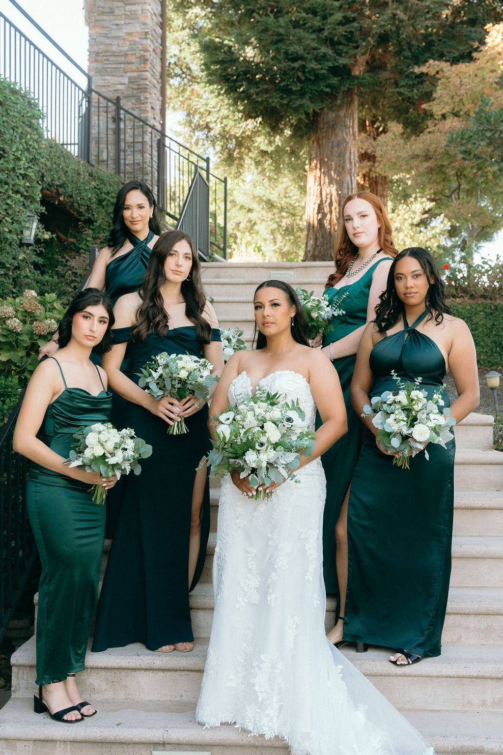 Bride posing with her bridesmaids in elegant green dresses on the grand staircase at Wolfe Heights