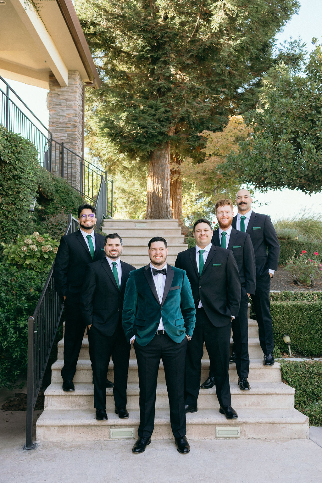 Groom standing with groomsmen in sharp black suits and green ties on the staircase at Wolfe Heights Wedding.