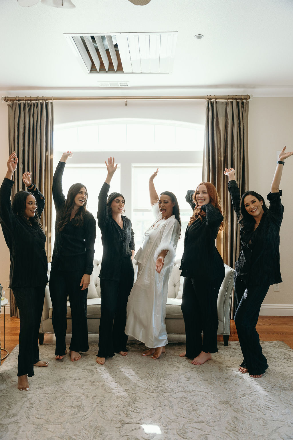 Bride and her bridesmaids in matching black loungewear, sharing laughter on a bed before the Wolfe Heights wedding