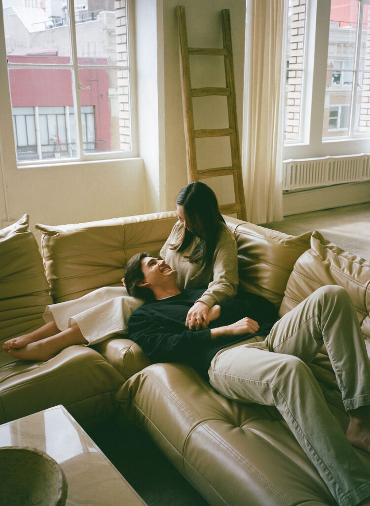 Cozy moment of a couple laughing together on a couch, taken on 35mm film during a DTLA studio engagement session.