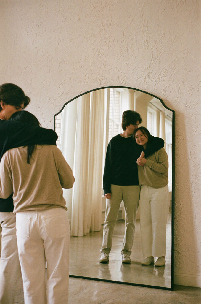 Silhouetted couple standing by a large studio window, framed by soft curtains, taken on 35mm film.