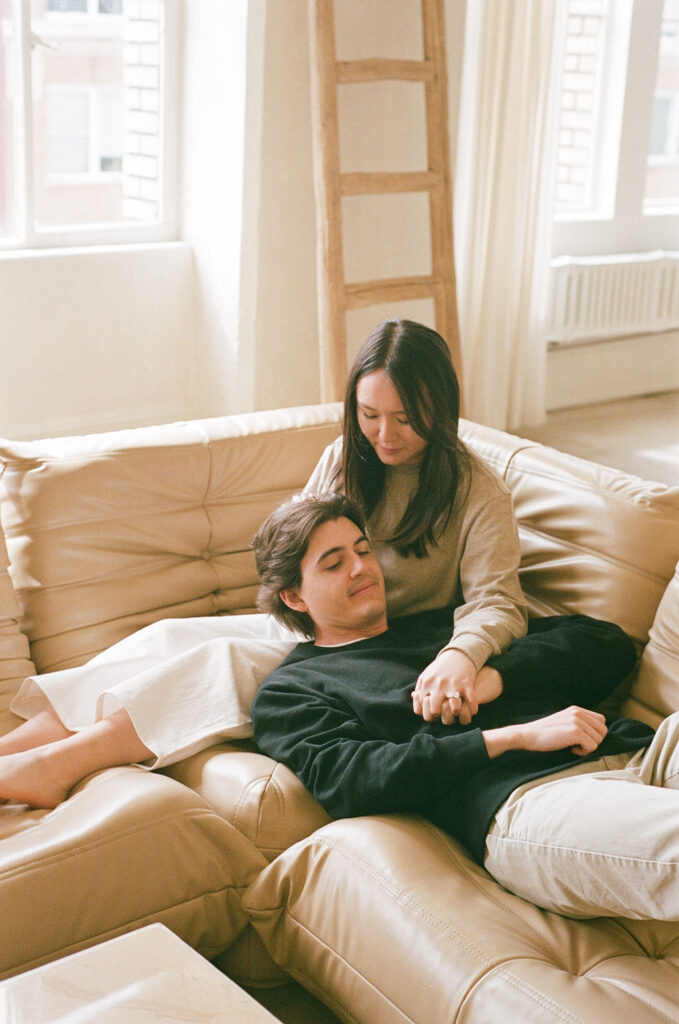 Couple embracing on a tan leather couch, bathed in soft window light, captured on 35mm film in a DTLA studio.