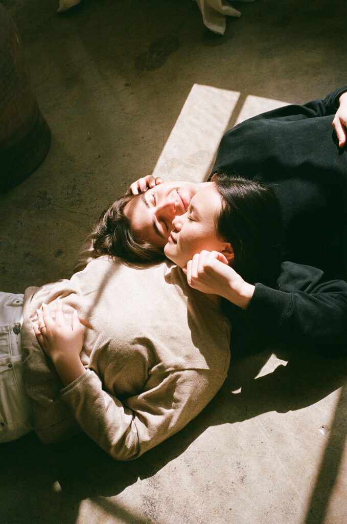 Couple lying in warm sunlight on the floor, framed by soft shadows in a DTLA studio engagement session on 35mm film.