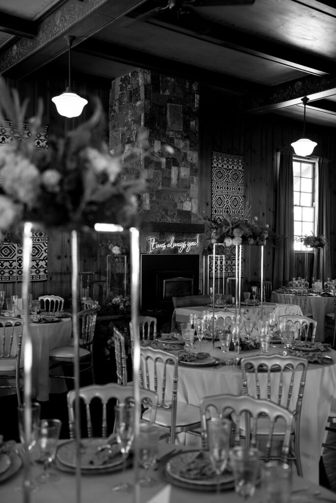 Black and white image of a rustic wedding reception hall with elegant decor and floral accents.