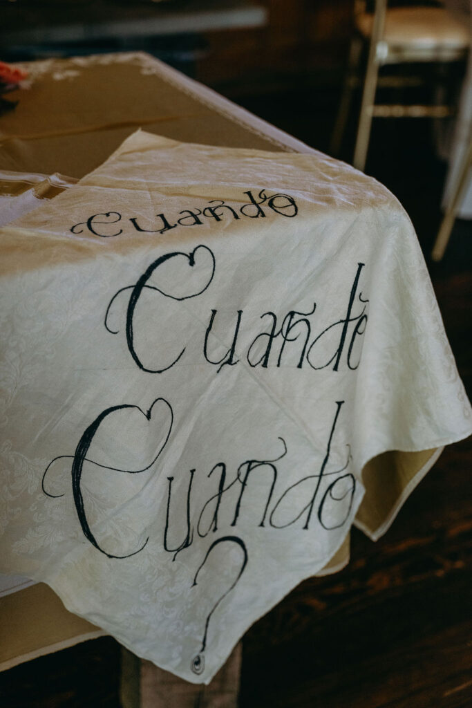 Handwritten "¿Cuándo, Cuándo?" tablecloth detail at a rustic wedding reception.