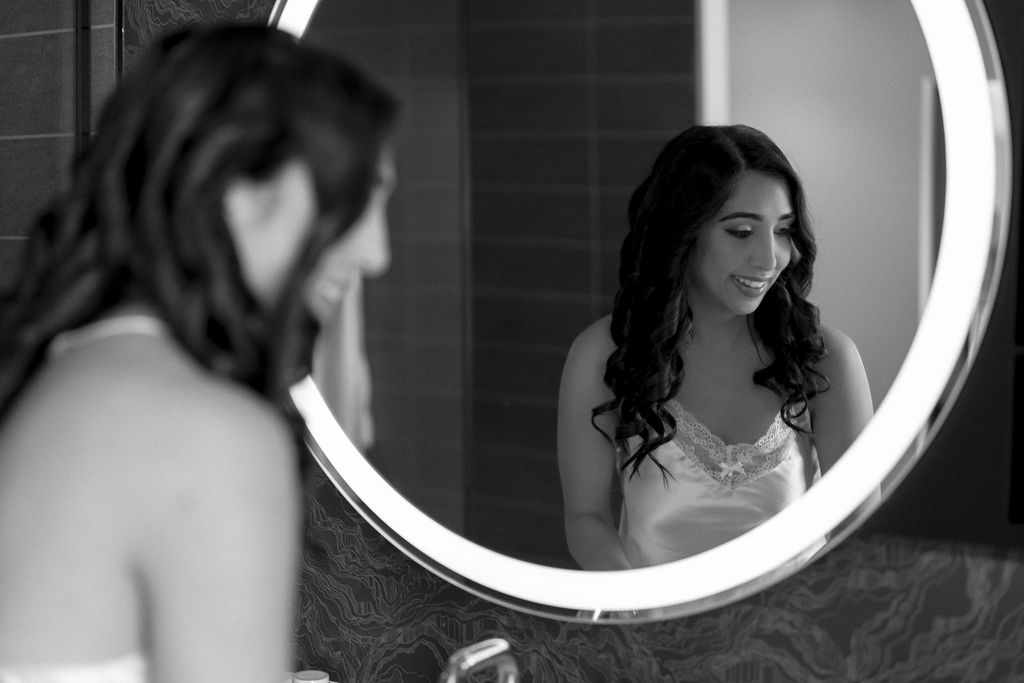 Bride smiling as she sees her wedding hair and makeup completed as she gets ready. 