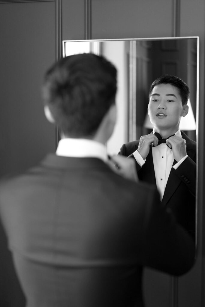 Groom adjusting his bow tie in the mirror before his wedding in Sacramento