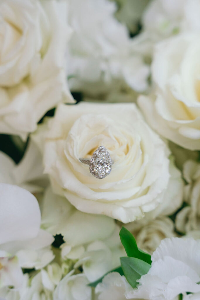 Close-up of a pear-shaped diamond engagement ring nestled in white roses during a Los Angeles proposal.