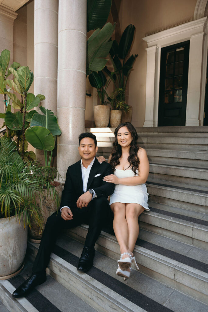 ViLan and Jason sit on the grand steps of The Guild Hotel, blending classic elegance with a bar engagement session