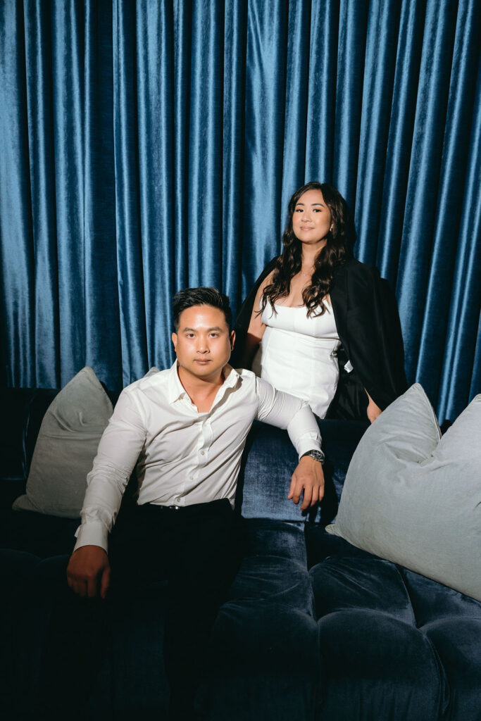 ViLan and Jason pose in front of deep blue velvet curtains during their stylish bar engagement session.