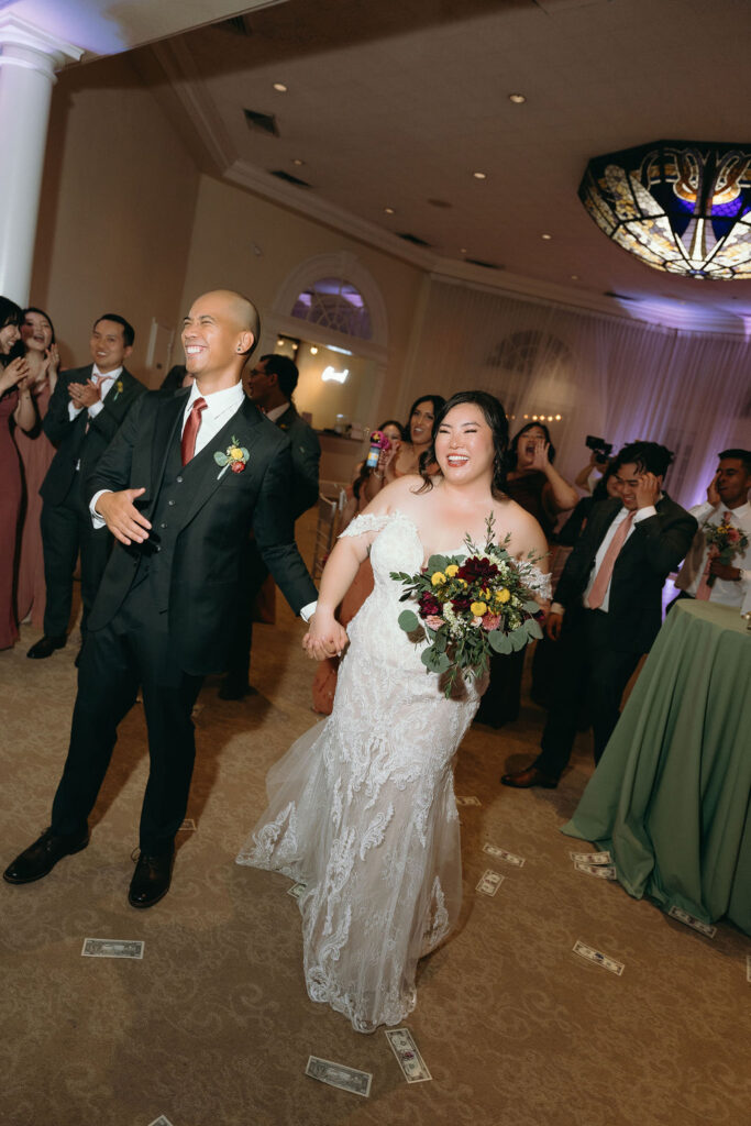 Bride and groom enter the reception at Vizcaya Sacramento, surrounded by cheering guests and a stained-glass ceiling