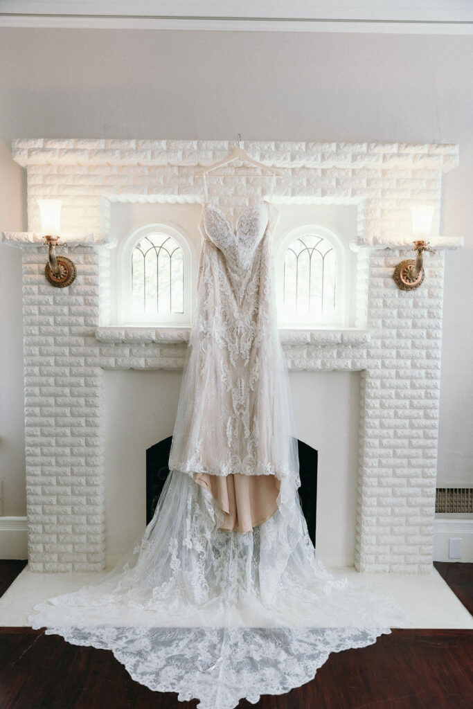 Lace wedding dress hanging on a white brick fireplace in the bridal suite at Vizcaya Sacramento