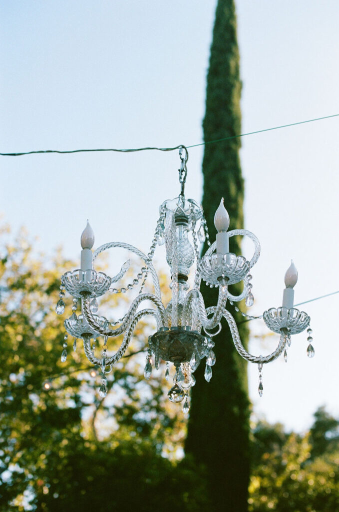 Crystal chandelier hanging outdoors at Vizcaya Sacramento, reflecting soft evening light against a green backdrop