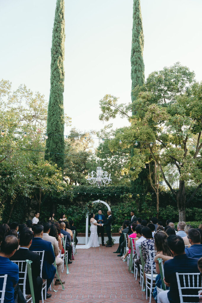 Outdoor wedding ceremony at Vizcaya Sacramento with towering cypress trees and a white floral arch