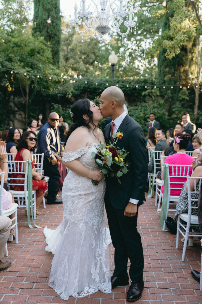 Bride and groom kiss down the aisle under a chandelier at their Vizcaya Sacramento wedding ceremony