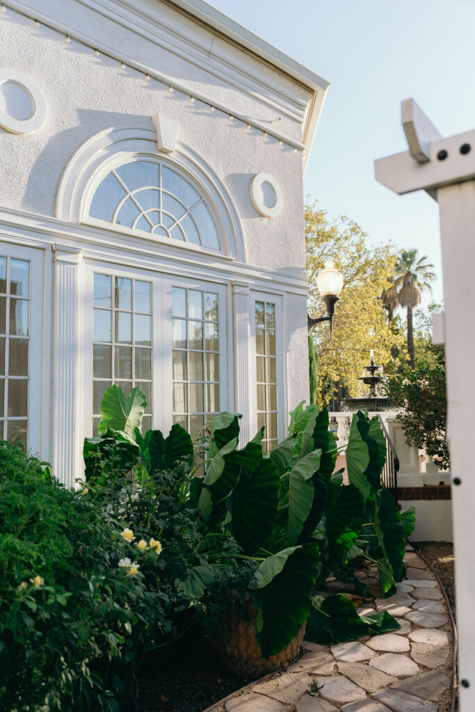 Elegant white building with tall arched windows at Vizcaya Sacramento, framed by lush greenery.