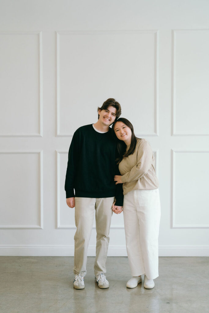 Couple posing against a white panel wall in a minimalist studio engagement session.