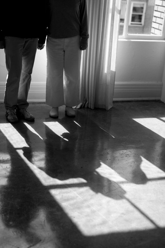 Couple standing in front of window focusing on their shadow silhouette in this studio engagement session in Los Angeles 