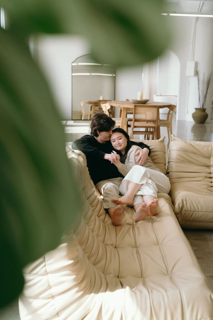 Cozy moment of couple embracing on a couch, framed by a plant in a DTLA studio setting.