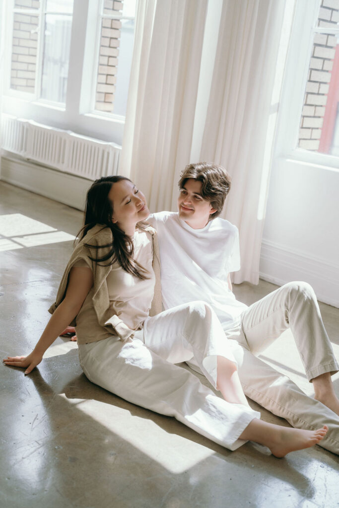 Couple sitting on the floor, reflected in a large mirror during their studio engagement session.