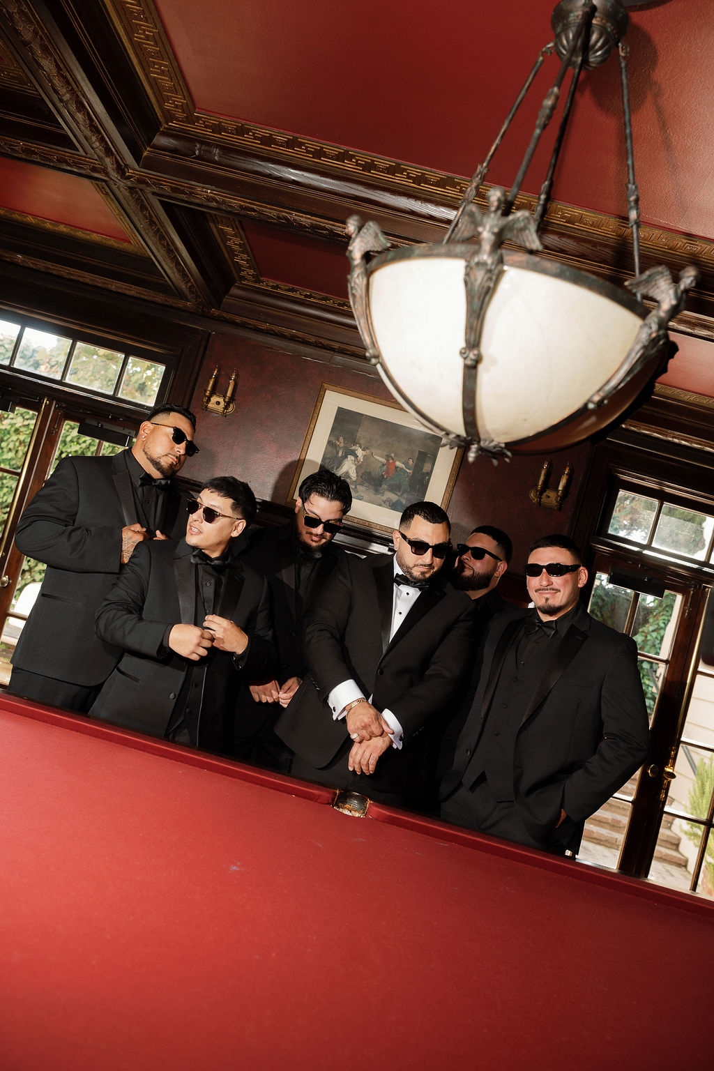 Groomsmen in black suits and sunglasses gathered by pool table at Grand Island Mansion.