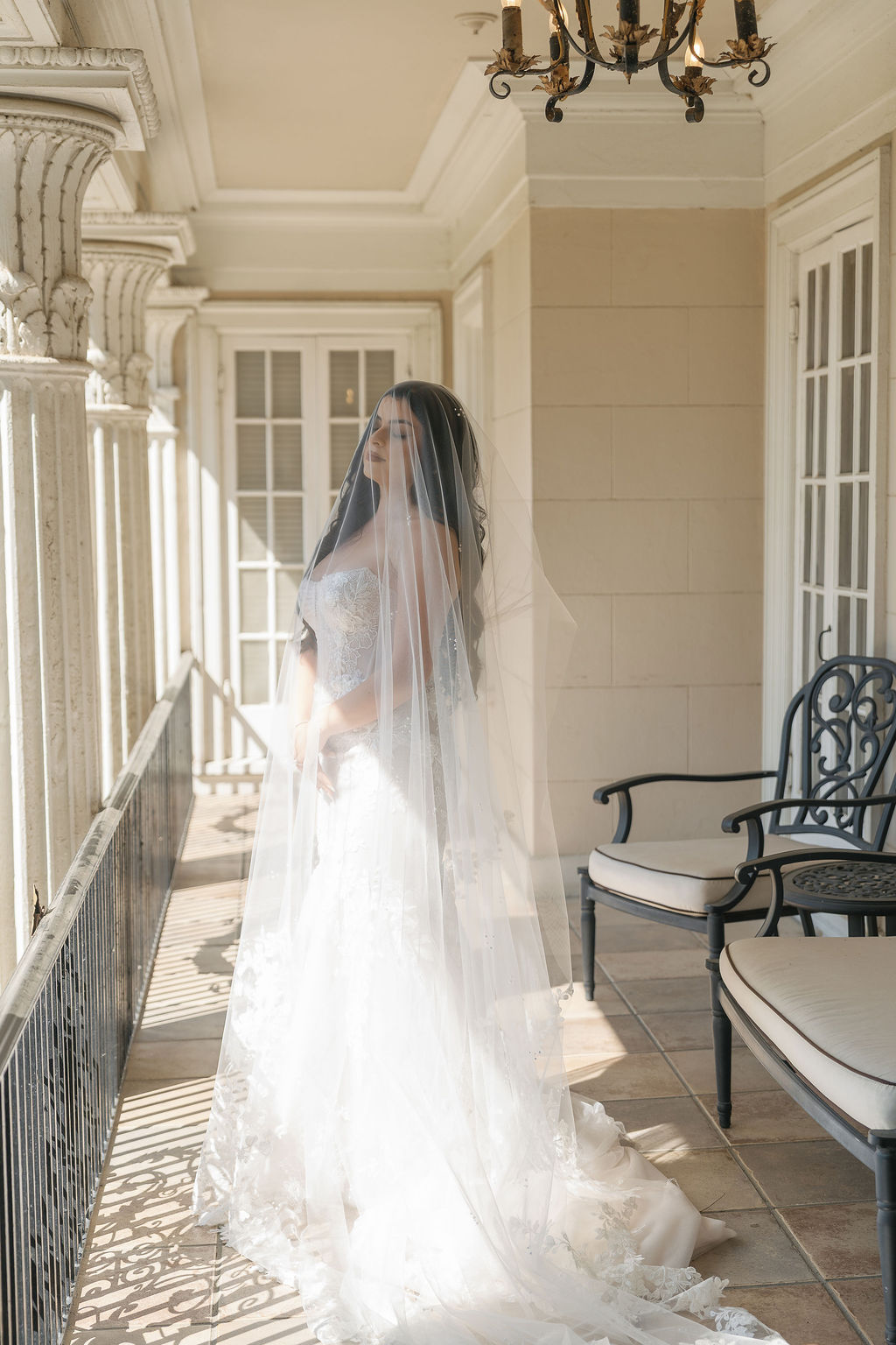 Bride in strapless gown with long veil standing on balcony at Grand Island Mansion.