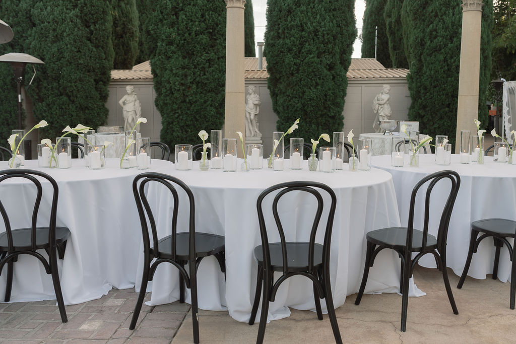 Serpentine tables with black chairs, candles, and calla lilies in courtyard at Grand Island Mansion.