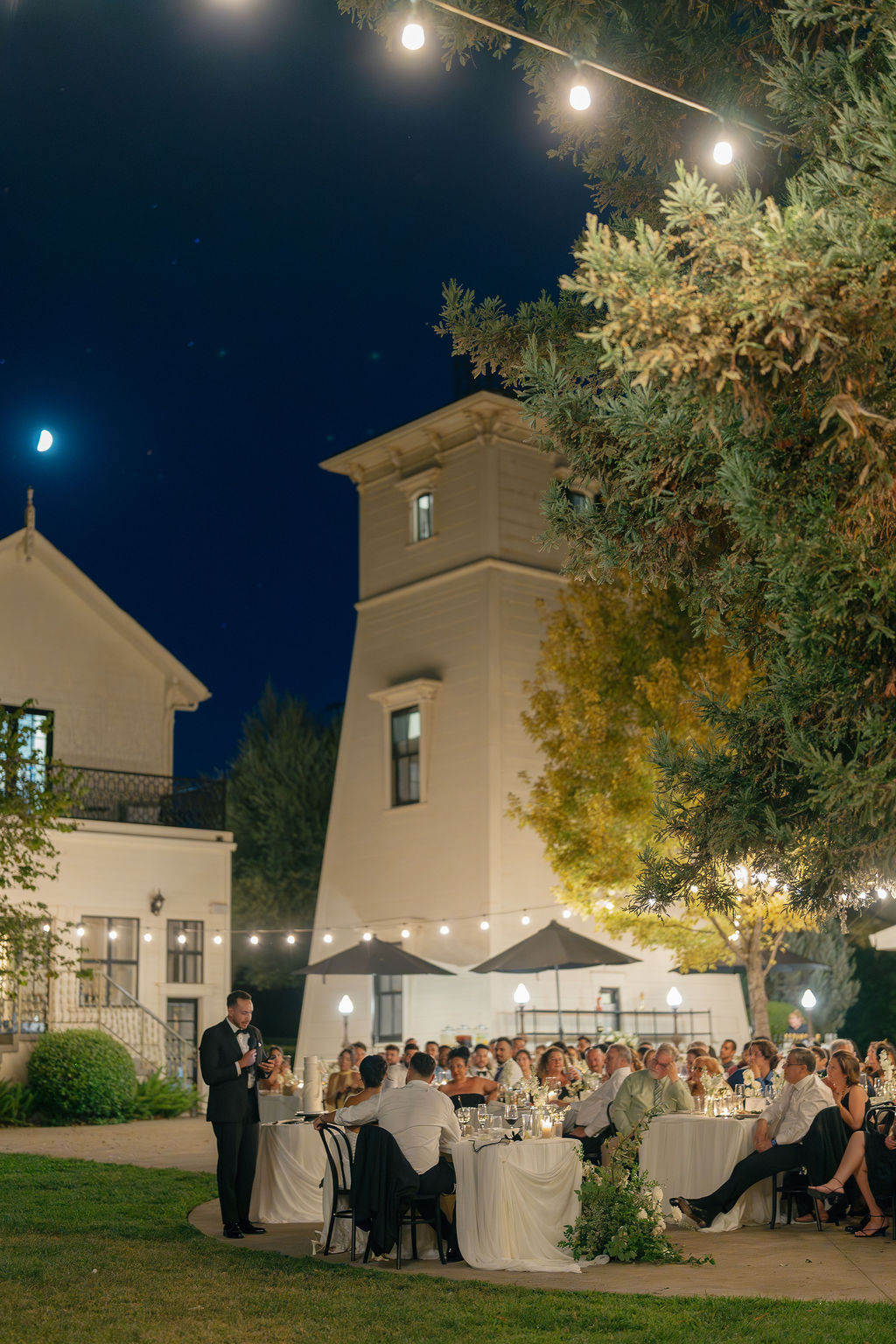 Evening wedding reception speeches under string lights at Park Winters venue.